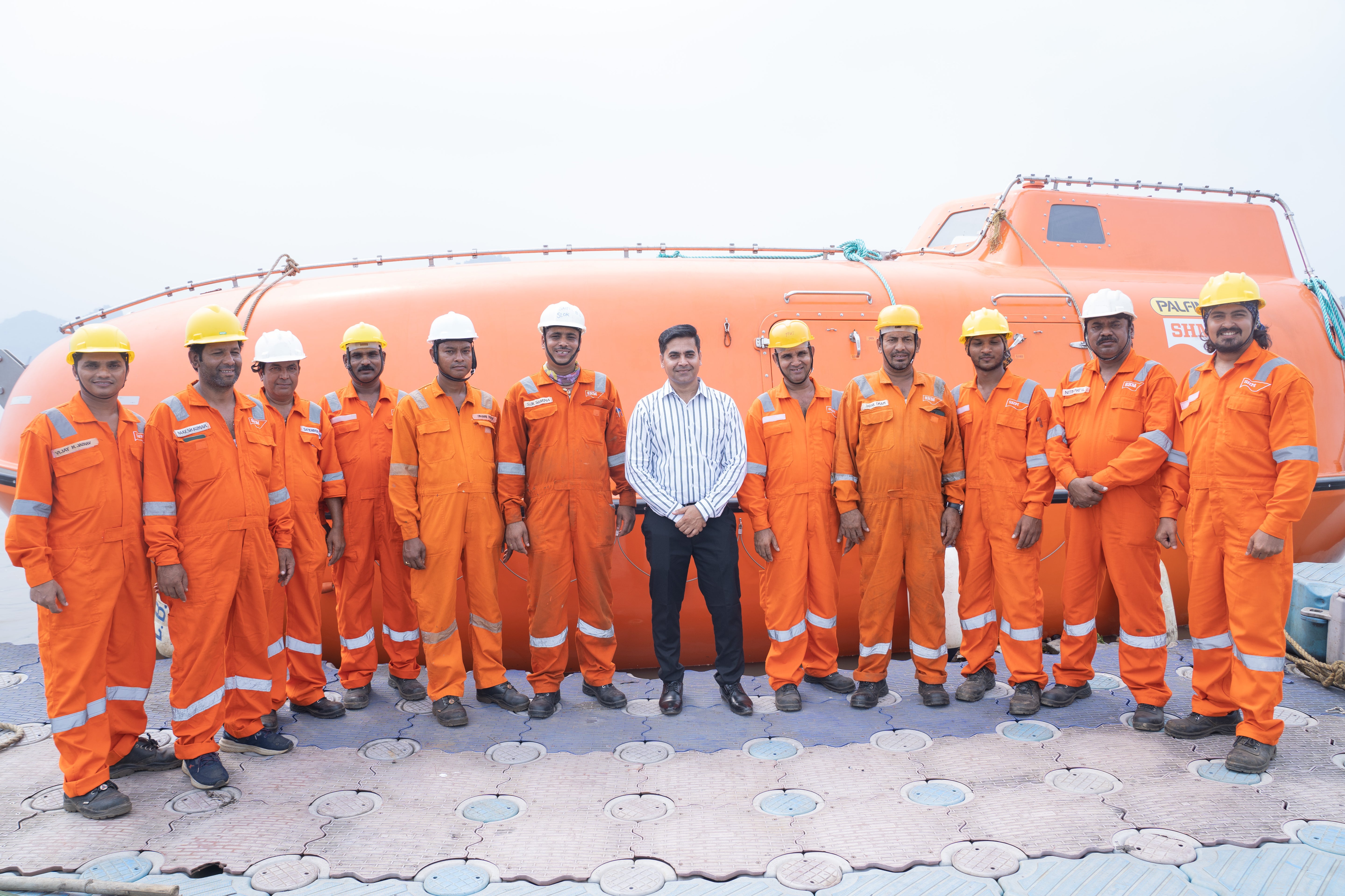 SHM Group's Maritime Safety Technician Team in orange boiler suit standing in front of an orange SHM lifeboat